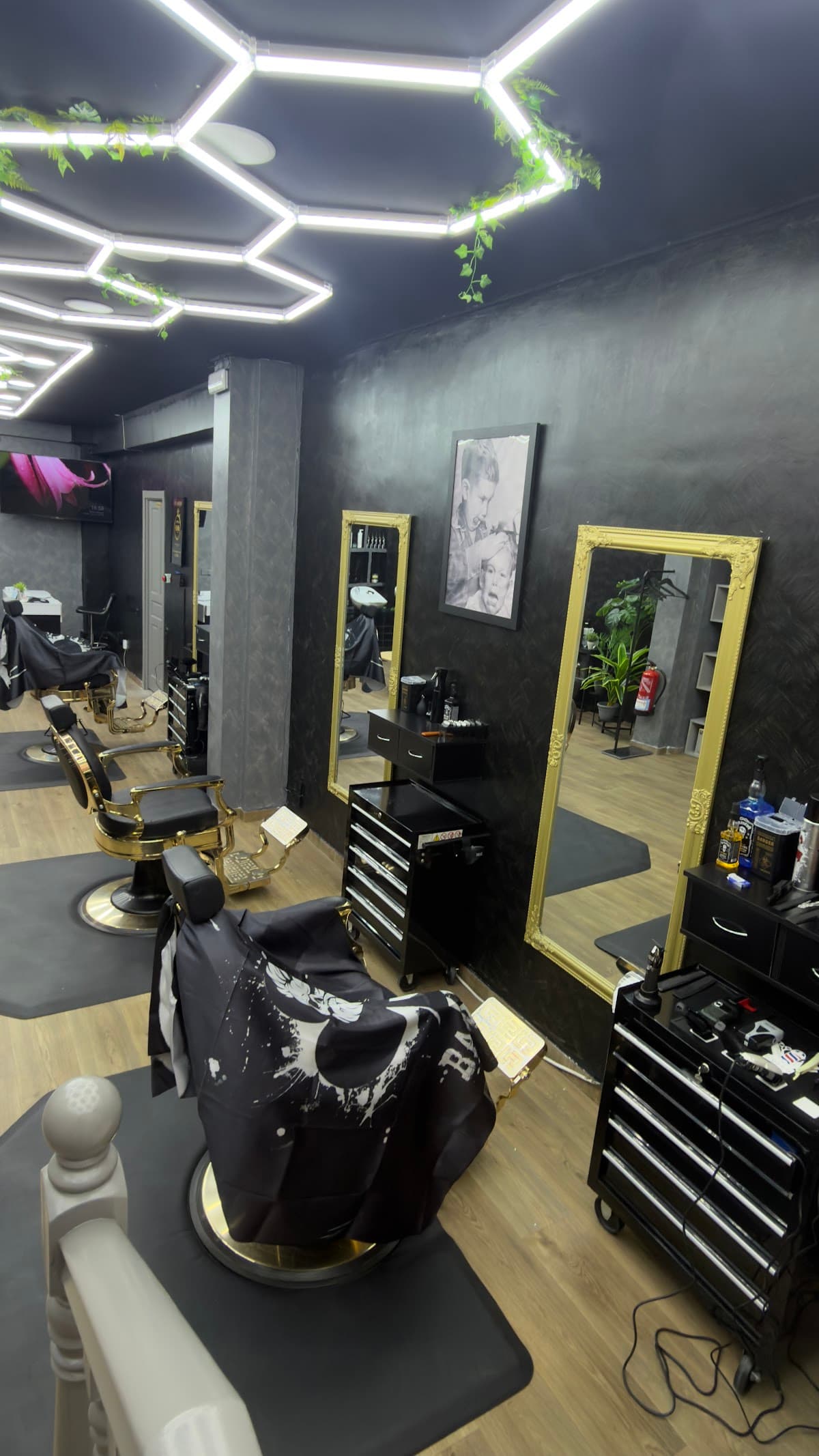 Sala principal de HB Barbers en Tarragona con espejos de marco dorado, sillones de barbero y luz cálida sobre suelo de madera