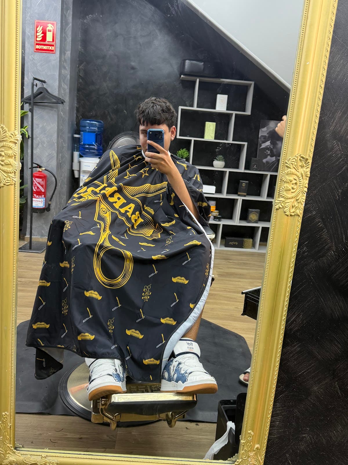 Cliente con capa de barbería HB Barbers reflejado en un espejo con marco dorado del local